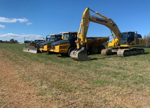 HGS Contracting excavator, haul trucks and dozer staged on a green field