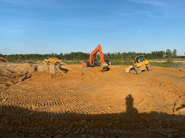Excavator and dozers cutting a stormwater basin at sunset