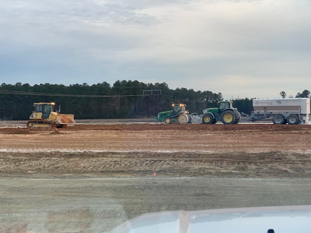 Soil stabilization tractors and dozer spreading material on a graded roadway