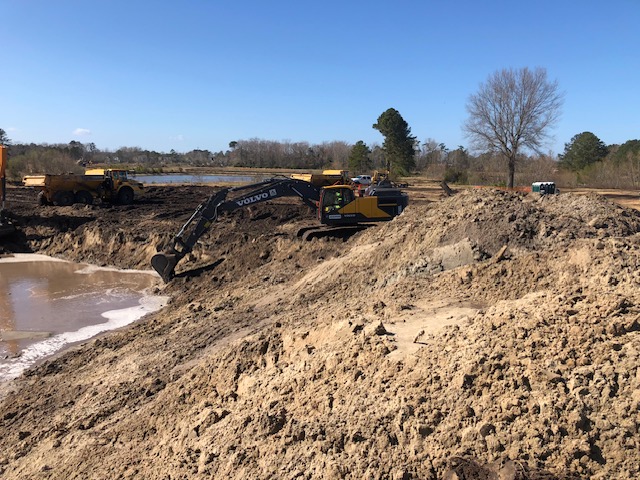 Volvo excavator shaping a detention basin beside a water feature